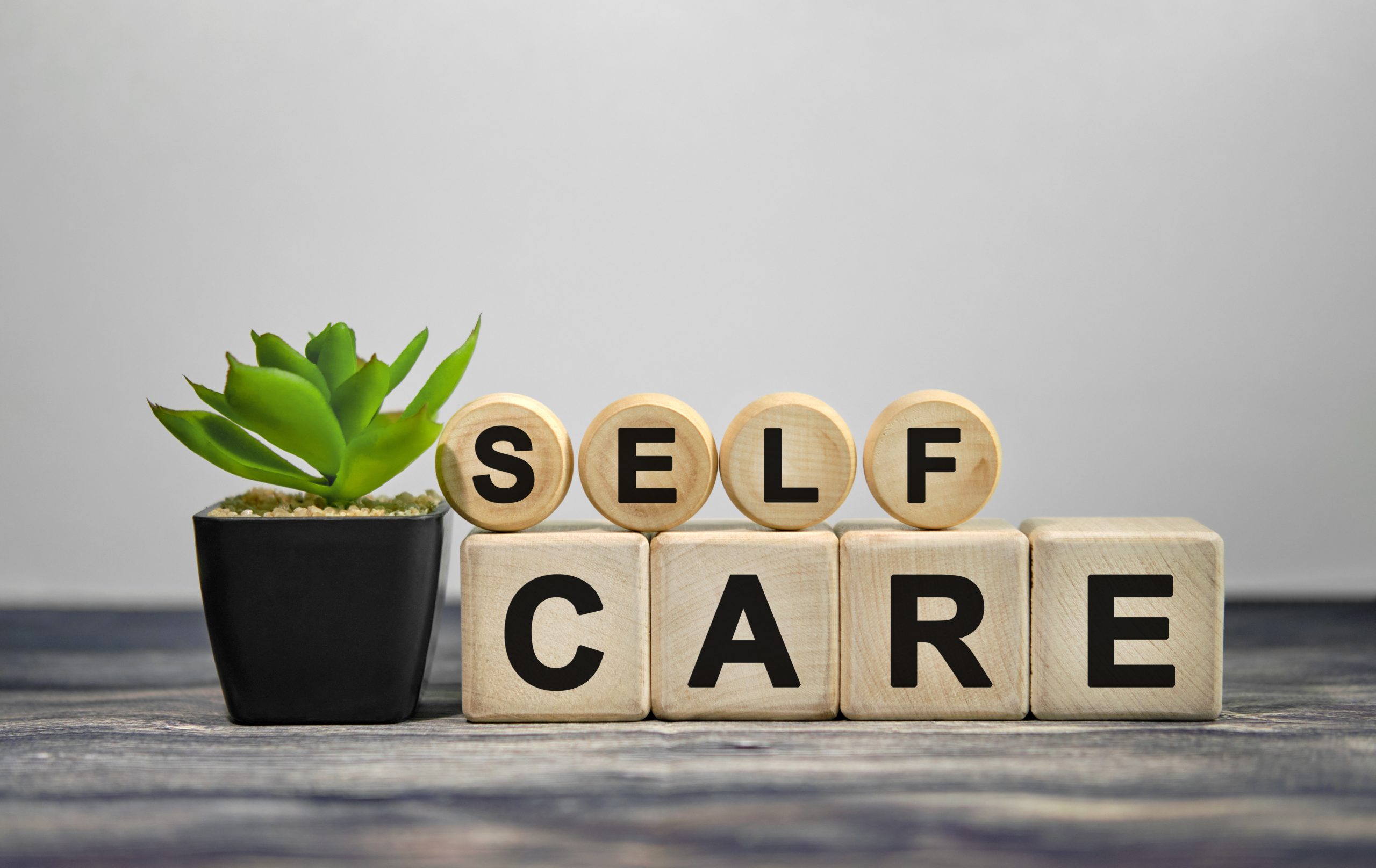 SELF CARE - text on wooden cubes, green plant in black pot on a wooden background